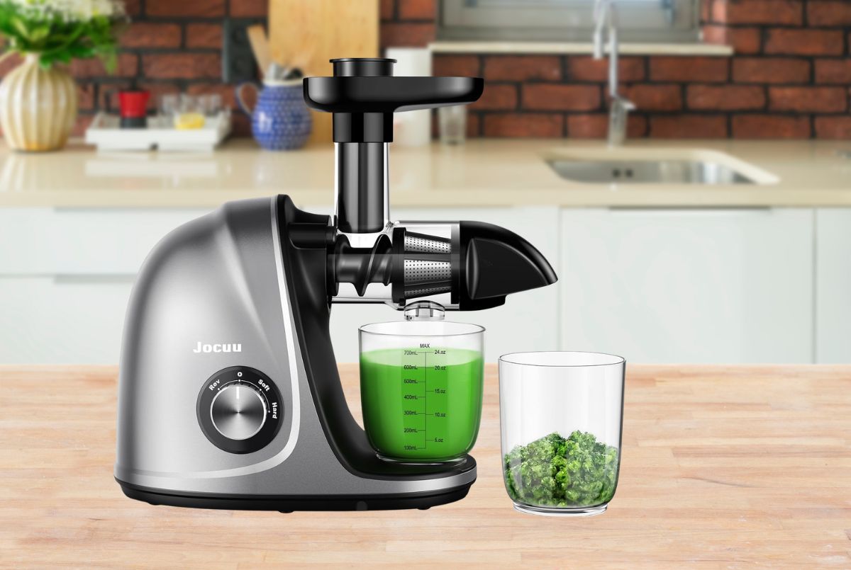 Jocuu Slow Masticating Juicer in teal with clear juice glass and dry pulp container on white marble