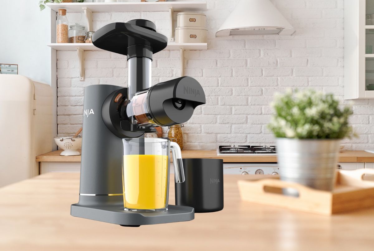 Ninja NeverClog Cold Press Juicer JC151 in charcoal with fresh celery and kale on white marble countertop
