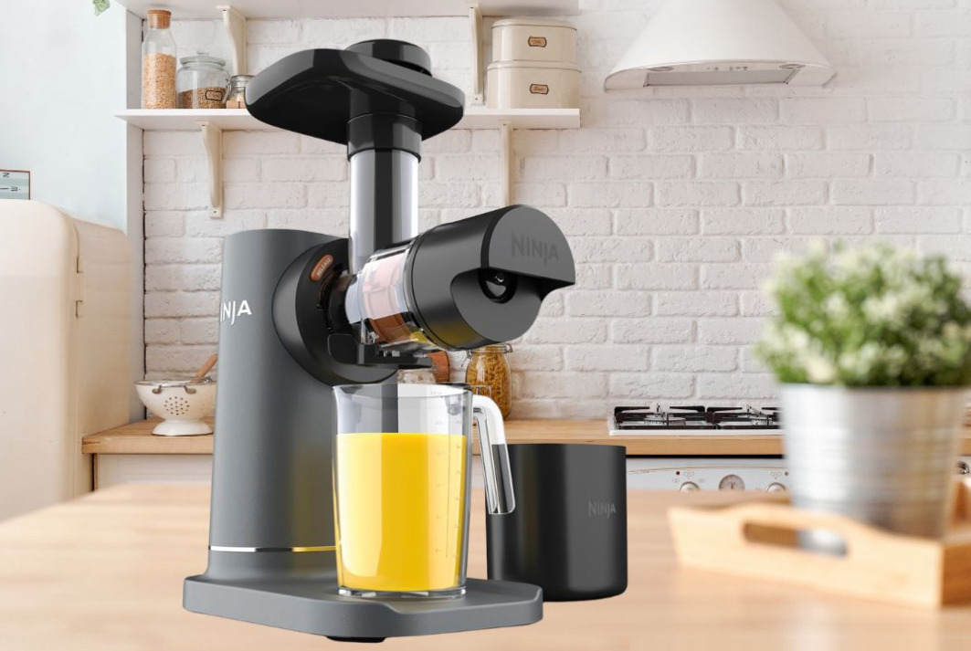 Ninja NeverClog Cold Press Juicer JC151 in charcoal with fresh celery and kale on white marble countertop